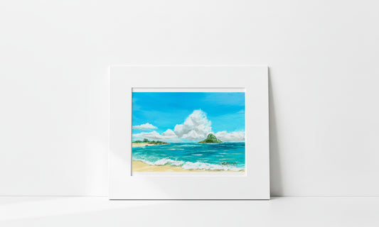 A matted landscape painting of a tropical beach with turquoise ocean water, white clouds, sandy shore, and green islands, displayed against a clean white wall.