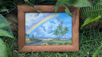 Framed painting of a Hawai'i landscape with a rainbow and palm trees on grass